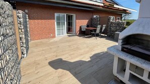 Ein Ziegelhaus mit einem Ziegeldach, eine Terrasse mit Grill und eine Steinmauer.
