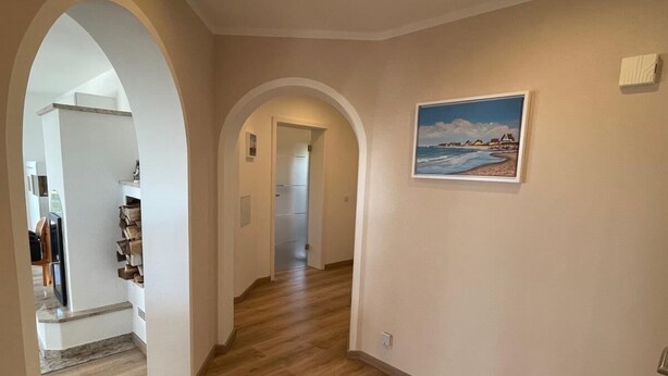 Un couloir avec un plancher en bois, des murs blancs et un tableau représentant une scène de plage.