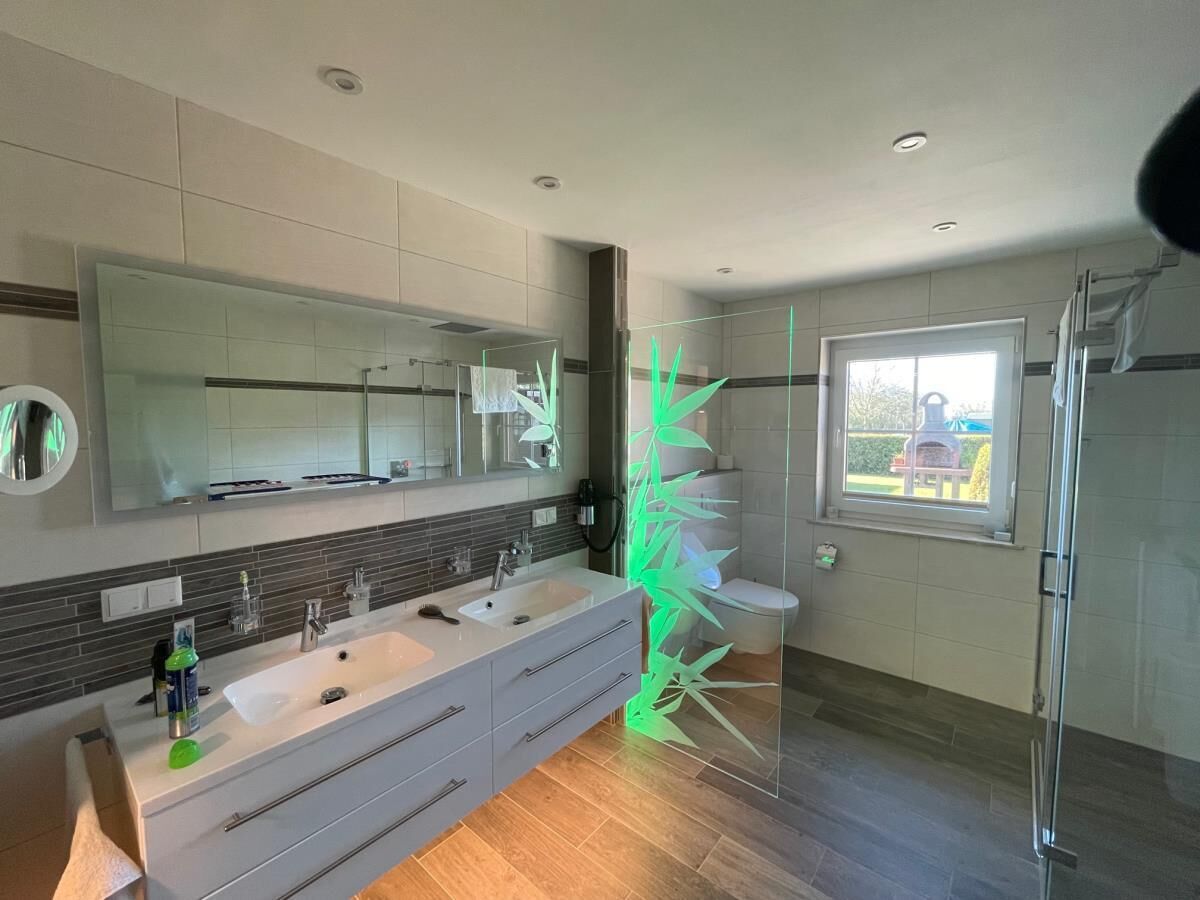A modern bathroom with a large mirror, two sinks, and a glass shower enclosure.