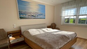 Une chambre à coucher avec un lit, des tables de chevet, une chaise, un tableau et une fenêtre.