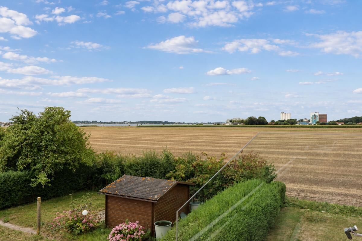 Ländliche Landschaft mit einer kleinen Holzhütte, einem Feld und Gebäuden in der Ferne.