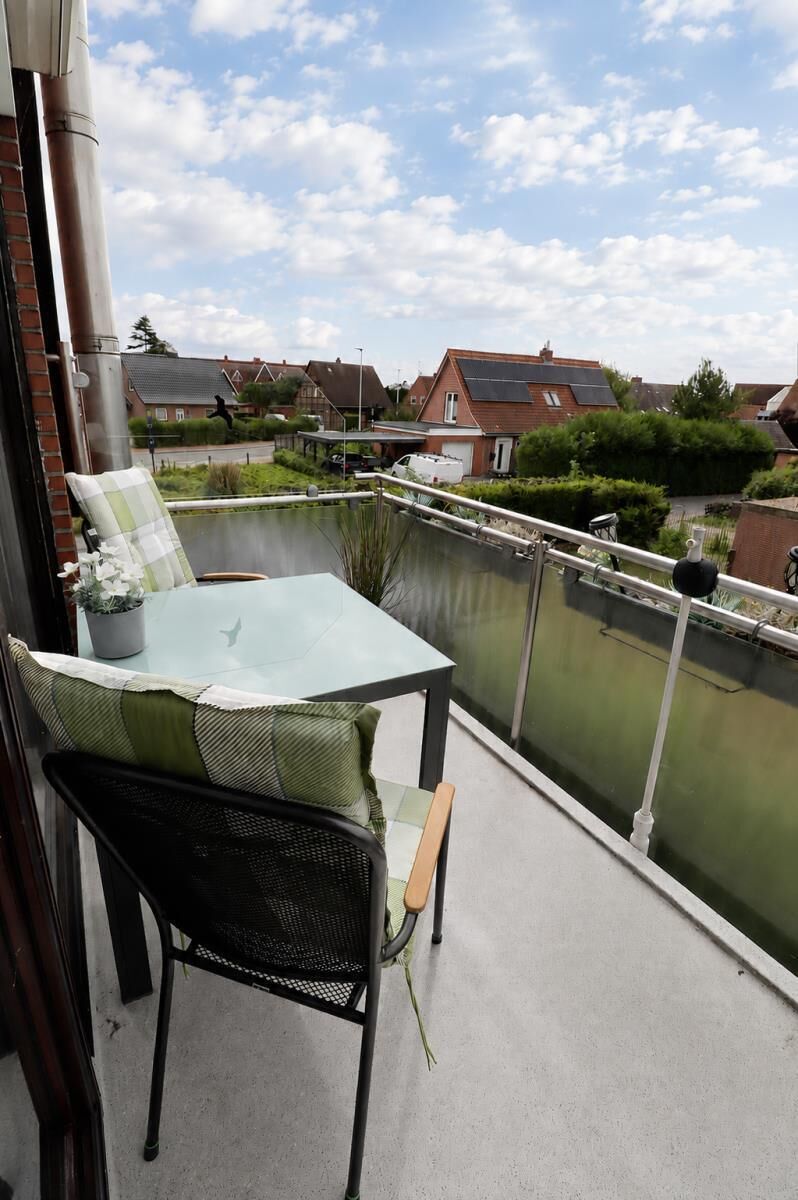 A balcony with a table and chairs, a potted plant, and a view of a residential area.