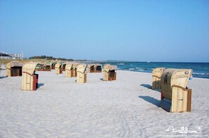 Des cabanes en osier, numérotées, sont disposées en rangées sur une plage de sable.