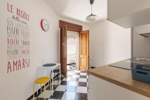 A modern kitchen with a checkered floor, a wooden door, a white wall with motivational text, a red clock, and a yellow stool. - Casa Tramonti - Trilo Comfort by BarbarHouse (Santa Maria di Leuca)