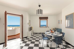 A dining area with a checkered floor, a table set for four, and a view of the sea through a window.