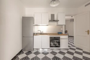 A compact kitchen with white cabinetry, a built-in oven, and a checkered floor.