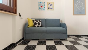 Una habitación con un sofá gris, dos cojines, un suelo a cuadros blanco y negro, y tres obras de arte en la pared.