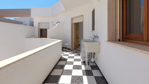 Un pasillo estrecho con piso de ajedrez, un lavamanos blanco y una zona de ducha.