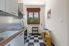Eine kleine Küche mit Schachbrettboden, einem Fenster mit Ausblick und einem kleinen Hocker.