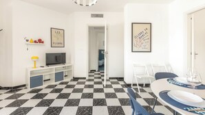 A modern living room with a checkered floor, a flat-screen TV, a dining area with a table and chairs, and two framed artworks on the walls. - Casa Tramonti - Trilo Superior by BarbarHouse (Santa Maria di Leuca)