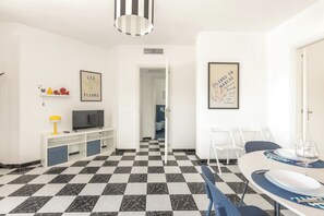 A modern living room with a checkered floor, a flat-screen TV, a dining area with a table and chairs, and two framed artworks on the walls. - Casa Tramonti - Trilo Superior by BarbarHouse (Santa Maria di Leuca)