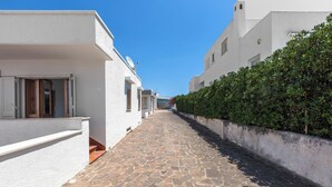 A narrow stone-paved street flanked by white buildings with balconies and a hedge on one side. - Casa Tramonti - Trilo Superior by BarbarHouse (Santa Maria di Leuca)