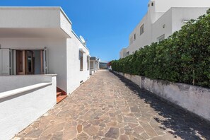 A narrow stone-paved street flanked by white buildings with balconies and a hedge on one side. - Casa Tramonti - Trilo Superior by BarbarHouse (Santa Maria di Leuca)