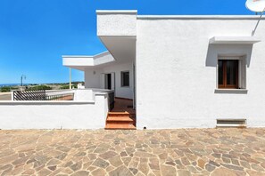 A modern building with a stone-paved entrance, a balcony, and a clear view of the sea. - Casa Tramonti - Trilo Superior by BarbarHouse (Santa Maria di Leuca)