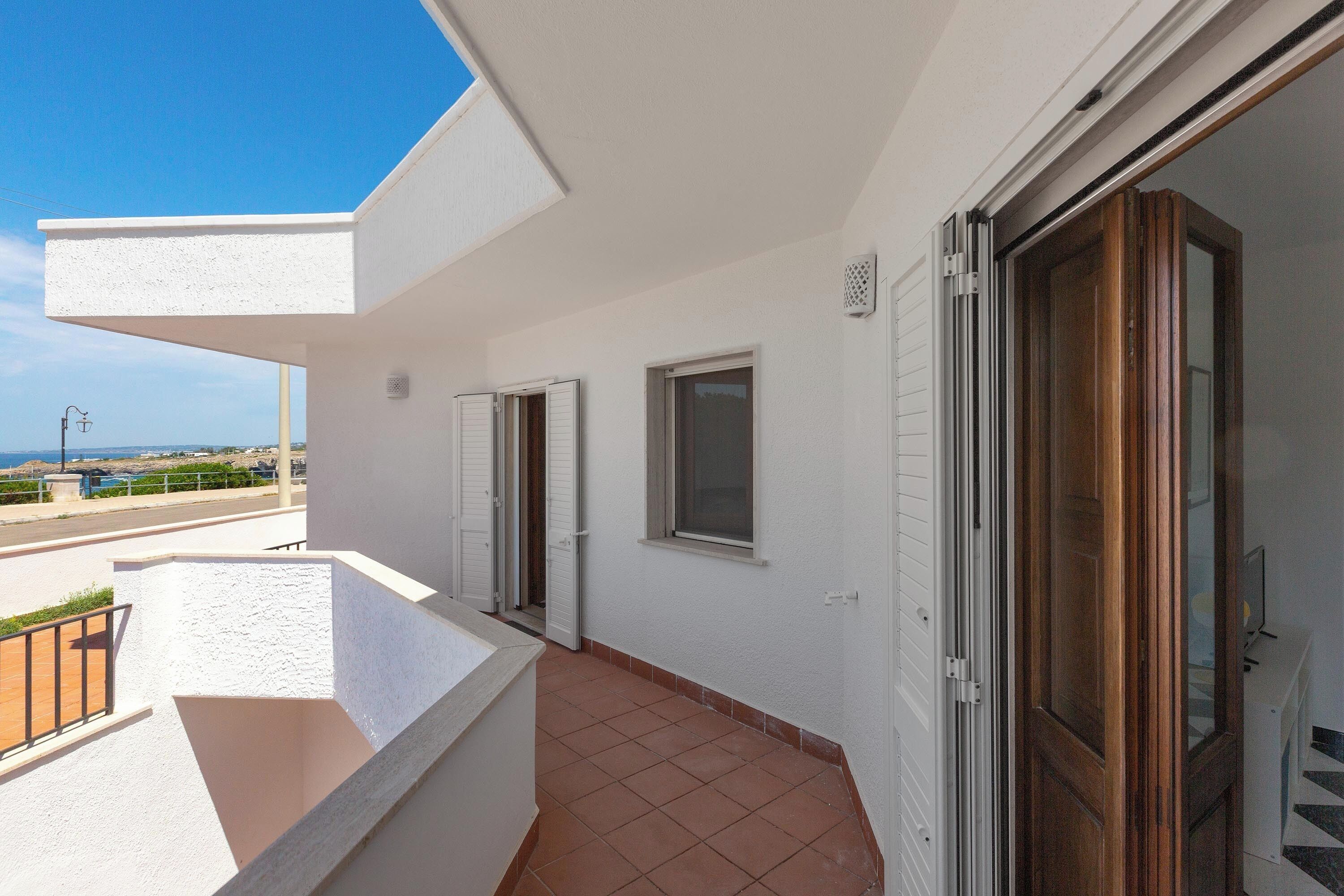 A balcony with a view of the sea, a door, and a window.
