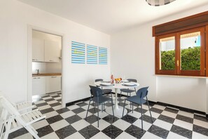 A dining area with a checkered floor, a round table, and four chairs. There is a window with a view of greenery outside. - Casa Tramonti - Trilo Superior by BarbarHouse (Santa Maria di Leuca)