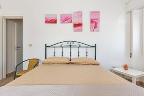 A bedroom with a bed, a chair, a bedside table, and a wall with three artworks. - Villetta Rosa dei Venti  by BarbarHouse (Torre Colimena)