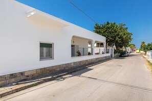 A white building with a flat facade, multiple windows, and a paved street. - Villetta Rosa dei Venti  by BarbarHouse (Torre Colimena)