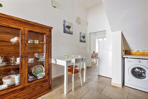 A kitchen with a wooden cabinet, a dining table with chairs, and a washing machine. - Villetta Rosa dei Venti  by BarbarHouse (Torre Colimena)