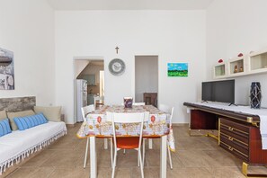 Een eethoek met een tafel gedekt voor vier personen, een keuken op de achtergrond, een televisie op een standaard en een kruis aan de muur.