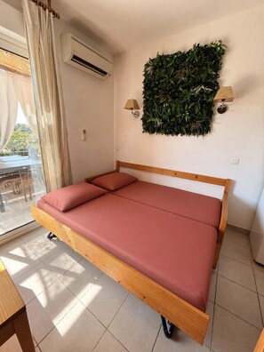 A bedroom with a bed, an air conditioning unit, a wall-mounted plant, and a window with curtains. - Apartment for 4 people in a complex with a pool, direct beach access, and a restaurant. (Poggio-Mezzana)