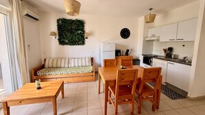 Un espace de vie compact comprenant un canapé, une table à manger, des chaises, un coin cuisine et un mur décoratif.