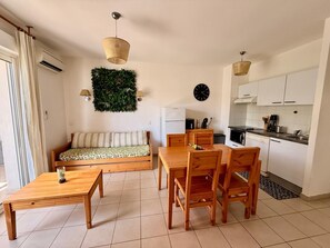 Ein kompakter Wohnraum mit einer Couch, Esstisch, Stühlen, einer Küchenzeile und einer Wanddekoration.