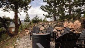 Ulkona on oleskelualue, jossa on Adirondack-tyylisiä tuoleja ja nuotiopaikka. Alue on kivien ja puiden ympäröimä.