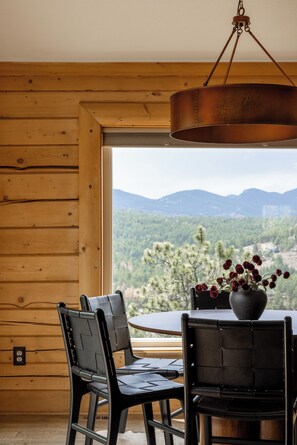 A wooden interior with a dining table and chairs, a hanging light fixture, and a view of a mountainous landscape through a window. - Log Cabin Retreat - Hot Tub · Sauna · Game Room · Stunning Mountain Views (Pine)