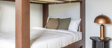 A bunk bed with a wooden frame, white bedding, and a patterned rug.