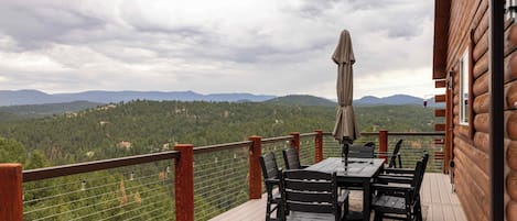 Une terrasse en bois avec une table et des chaises, offrant une vue sur un paysage montagneux.