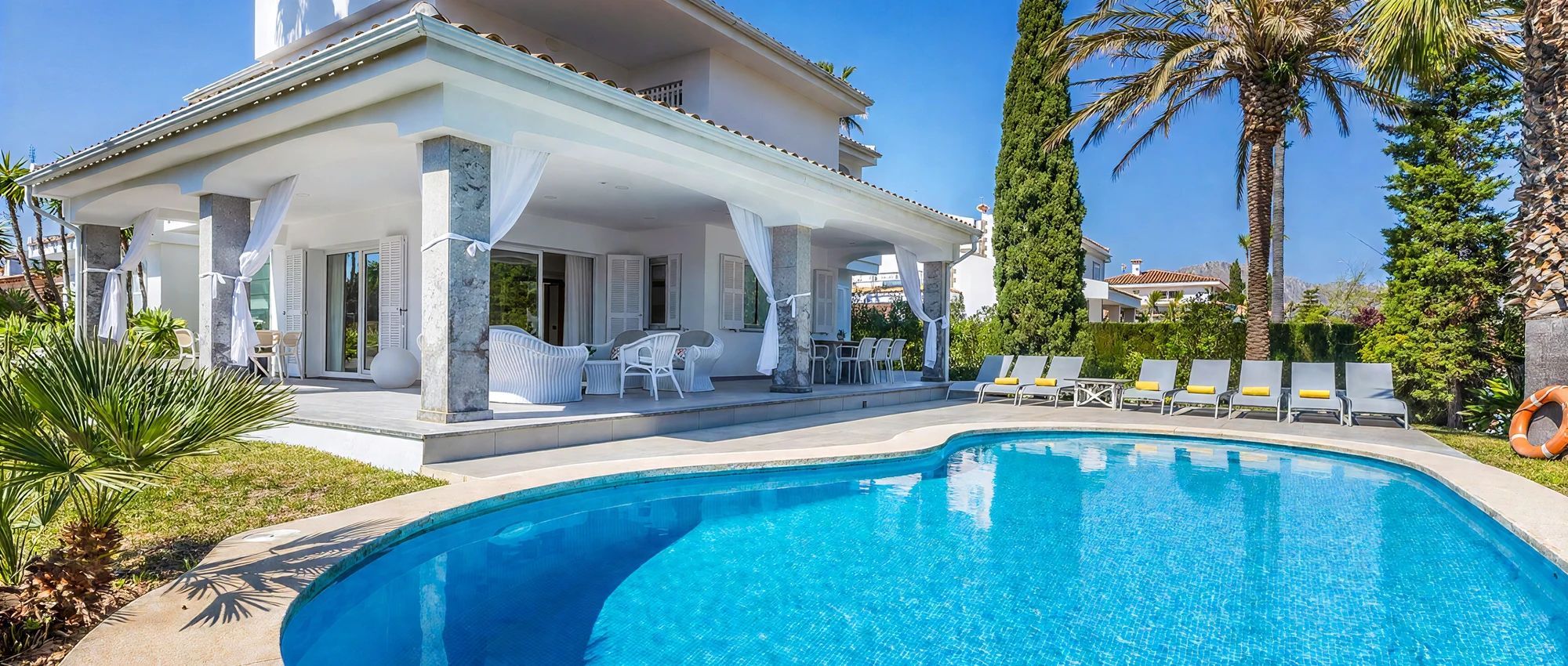 Zona de piscina con sillones de descanso y un espacio de estar techado.