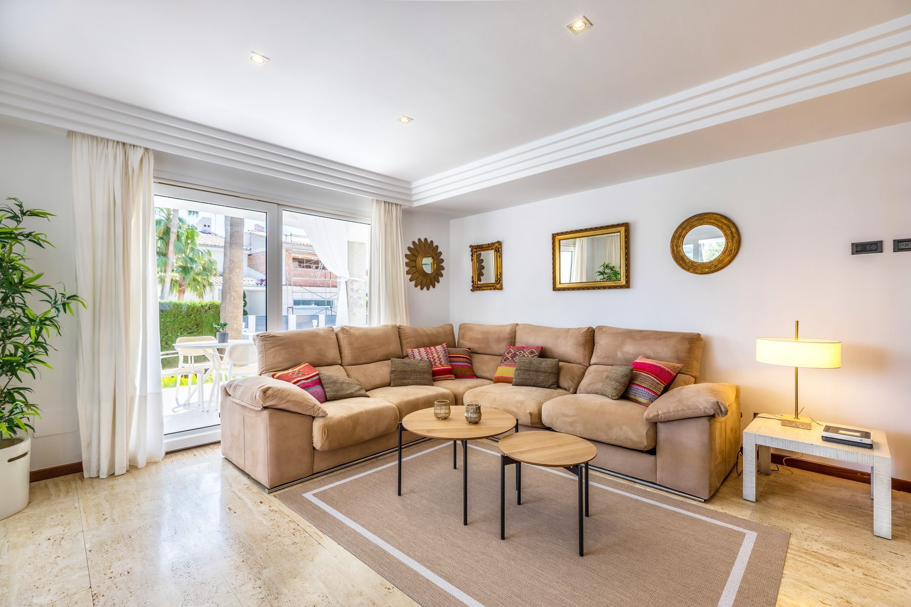 A modern living room with a beige sectional sofa, two small round tables, and a lamp.