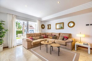 Ein modernes Wohnzimmer mit einem beige farbenen Ecksofa, zwei kleinen runden Tischen und einer Lampe.