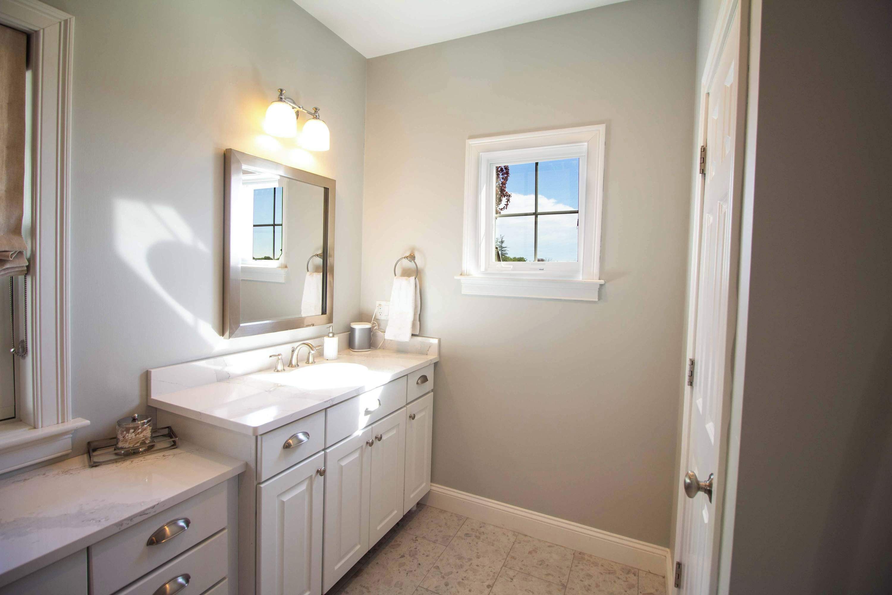 A bathroom with a double sink, a mirror, a window, and a door.
