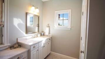 A bathroom with a double sink, a mirror, a window, and a door.