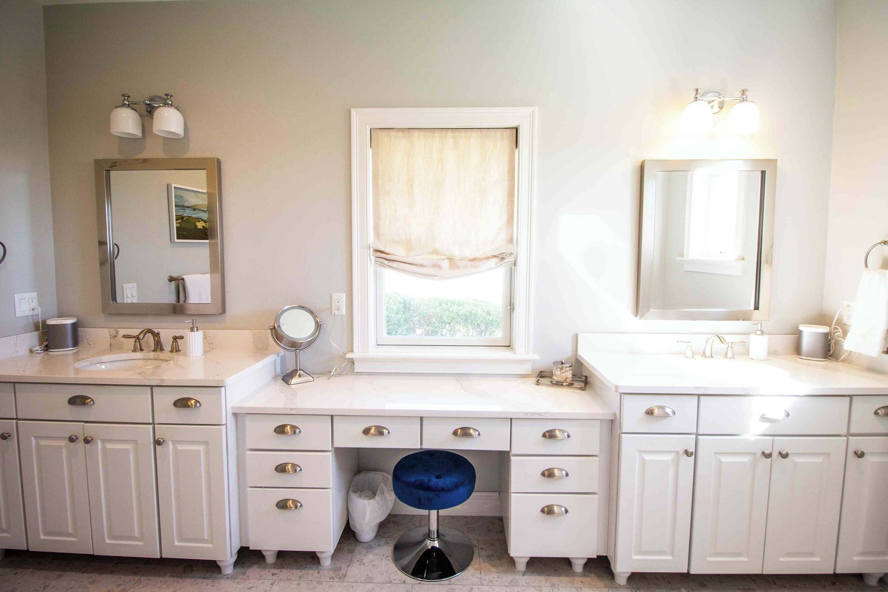 A bathroom with two sinks, a vanity with drawers, a mirror, and a window with curtains.