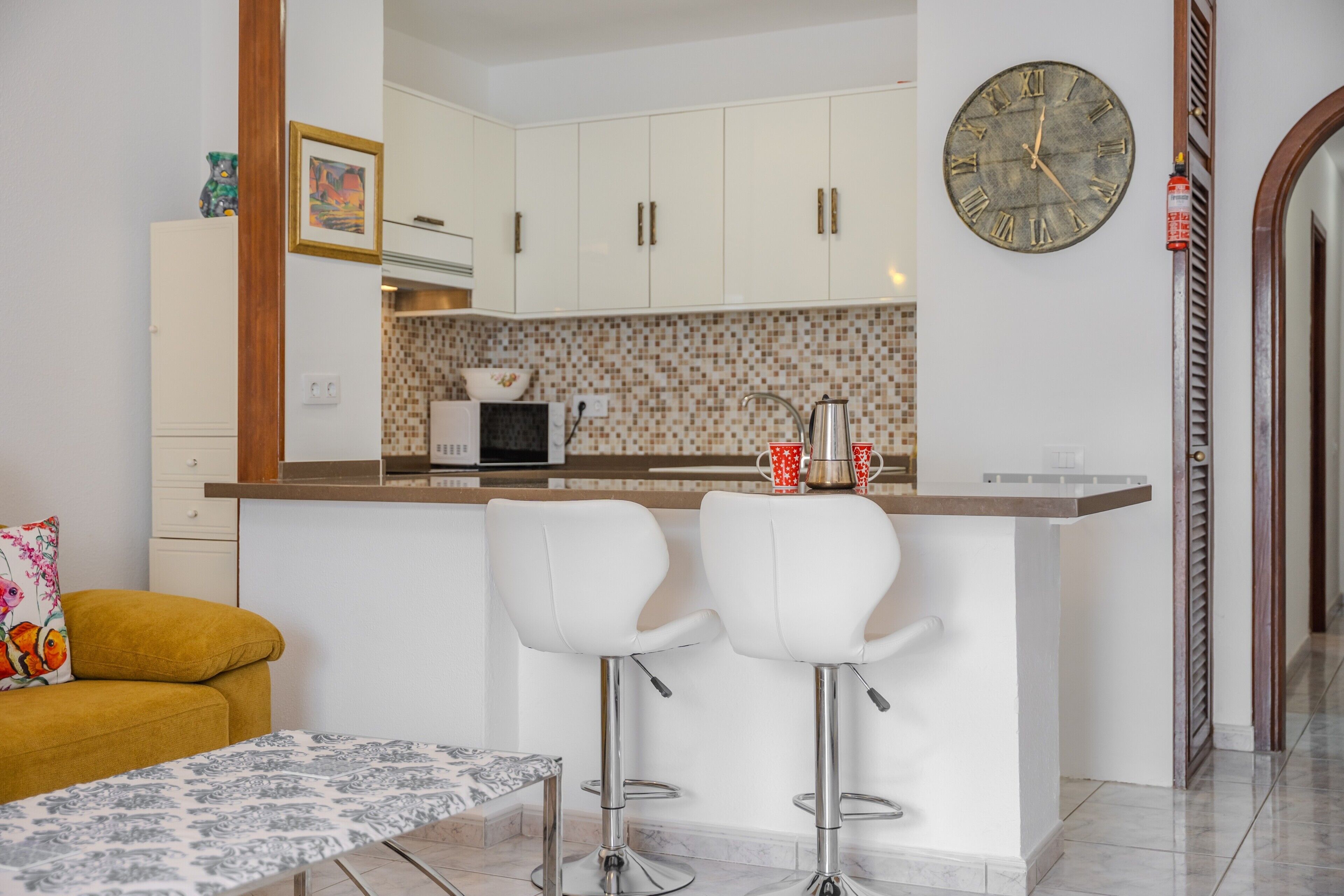 Een moderne keuken met witte kasten, een betegelde spatwand en een klok aan de muur.