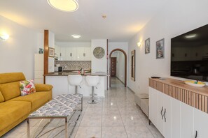 A modern kitchen with white cabinets, a dining area with a yellow sofa, and a hallway leading to a bedroom. - Vacation Apartment 'Victoria Court 2 51' with Shared Pool, Private Terrace and Wi-Fi (Arona)