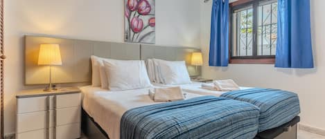 A hotel room with a bed, two bedside tables, a lamp, a painting, and a window with curtains.