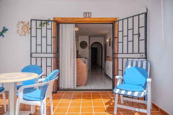 Una habitación con suelo de baldosas, una mesa con sillas, una cama y una puerta con el número indicado encima.
