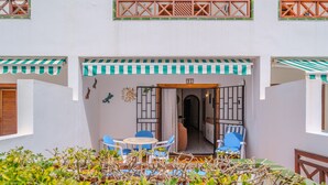 Un patio con una mesa y sillas, una puerta con un número y vista al interior.