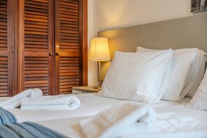 Una habitación de hotel con cama, almohadas, una mesita de noche con lámpara y puertas de madera.