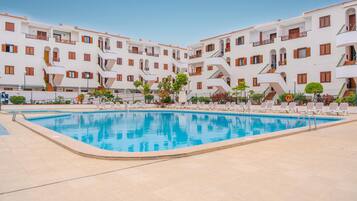 Une piscine entourée de bâtiments blancs dotés de balcons, sous un ciel dégagé.