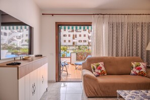 Una sala de estar con sofá, televisión y vista a una piscina y edificios.