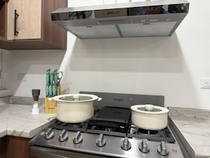 A kitchen with a gas stove, two pots, a range hood, and a set of knives.