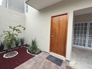 A wooden door with a metal handle, a welcome mat, and a small garden with various plants.
