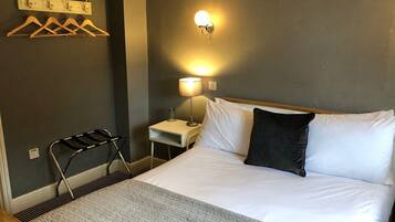 Habitación de hotel con cama, mesita de noche con lámpara, perchero y una silla.