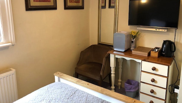 A hotel room with a bed, a desk with a computer, a chair, a television, and framed artwork on the wall. - Coachmakers Arms (Wallingford)