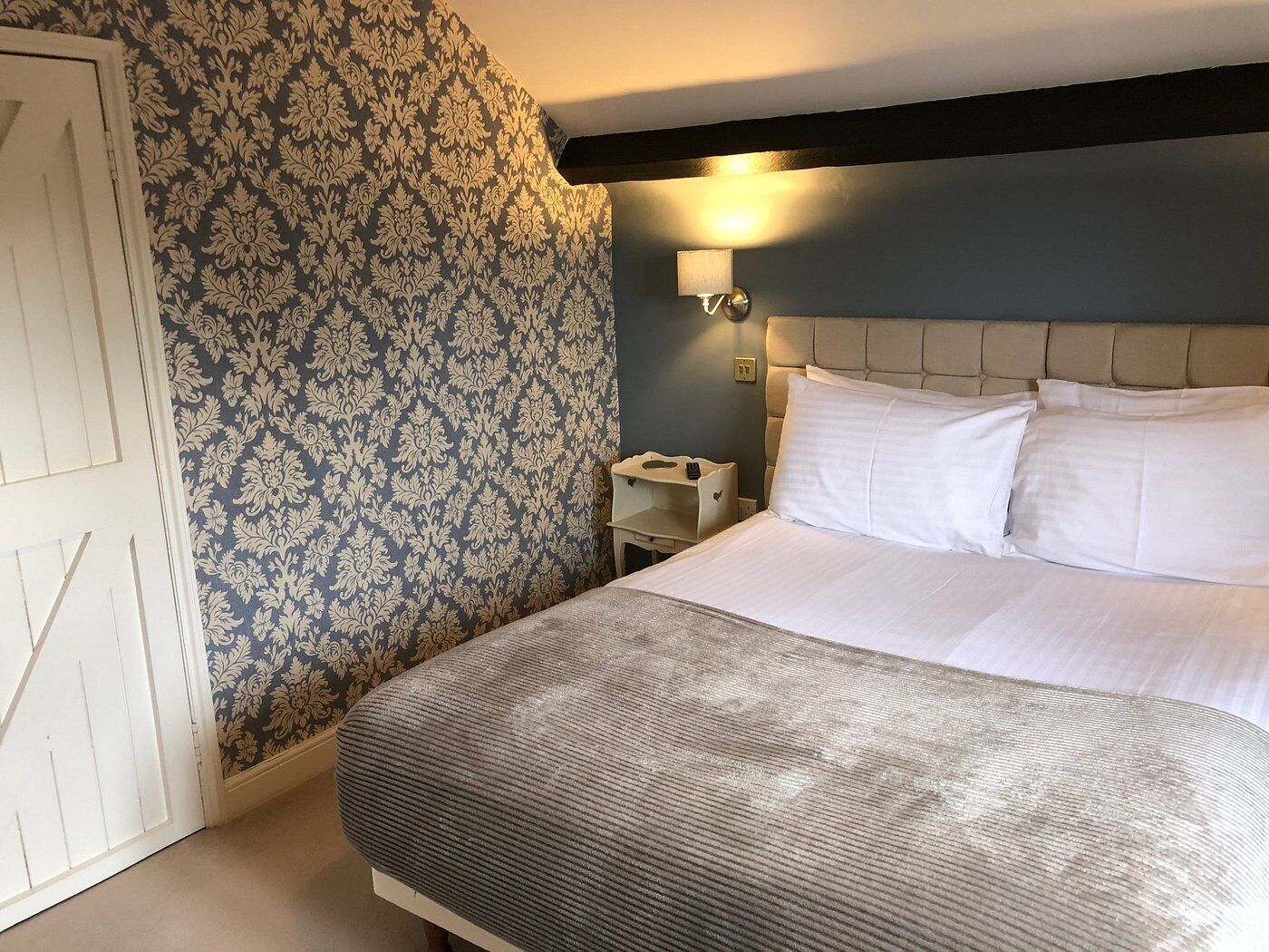 A hotel room with a bed, a nightstand, a wall-mounted lamp, and a patterned wallpaper.